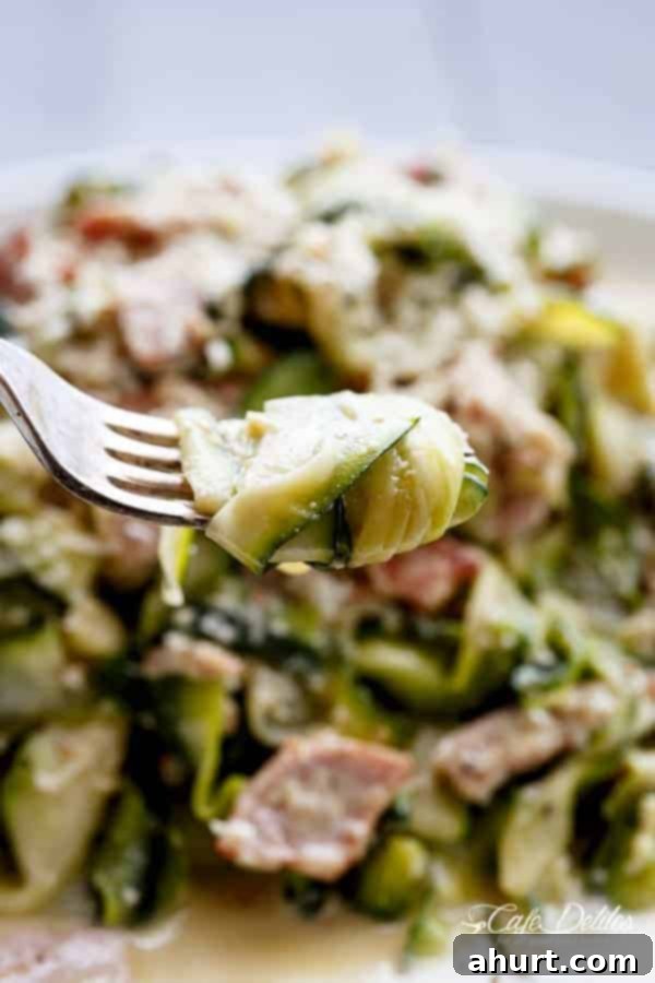 Zoodle Carbonara 12 A fork lifts a generous swirl of Zucchini (Zettuccine) Carbonara, showing the perfect coating of creamy sauce, crispy bacon, and tender zucchini ribbons.