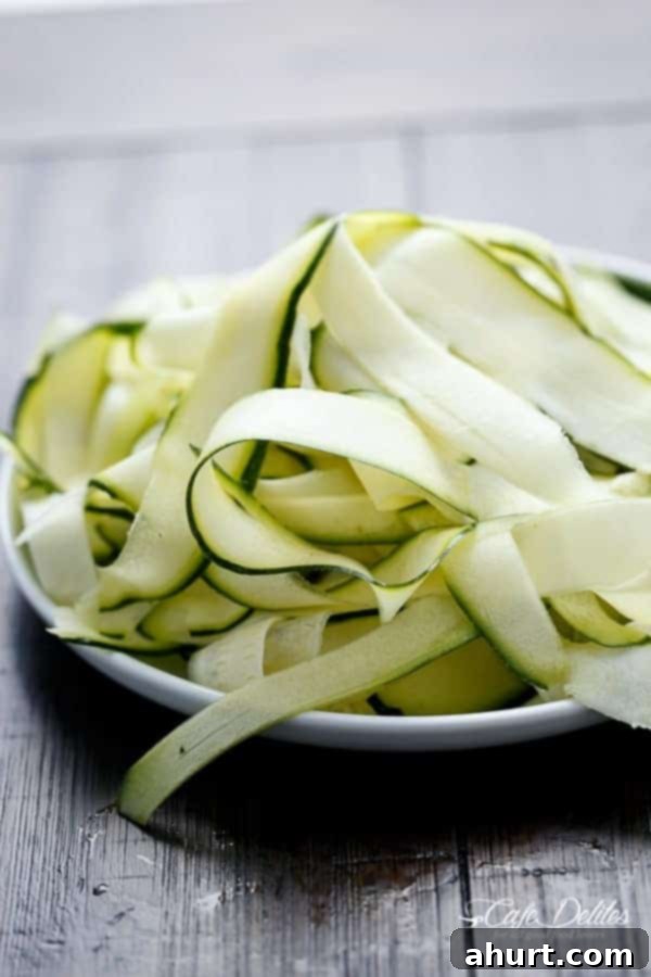 Zoodle Carbonara 5 A serving of Zucchini (Zettuccine) Carbonara on a white plate, showcasing the ribbons coated in sauce, with a few fresh herbs as garnish.