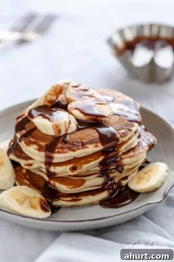 Gooey Nutella Banana Pancake Bliss 2 Nutella Stuffed Banana Pancakes with maple syrup stack on each other on a plate