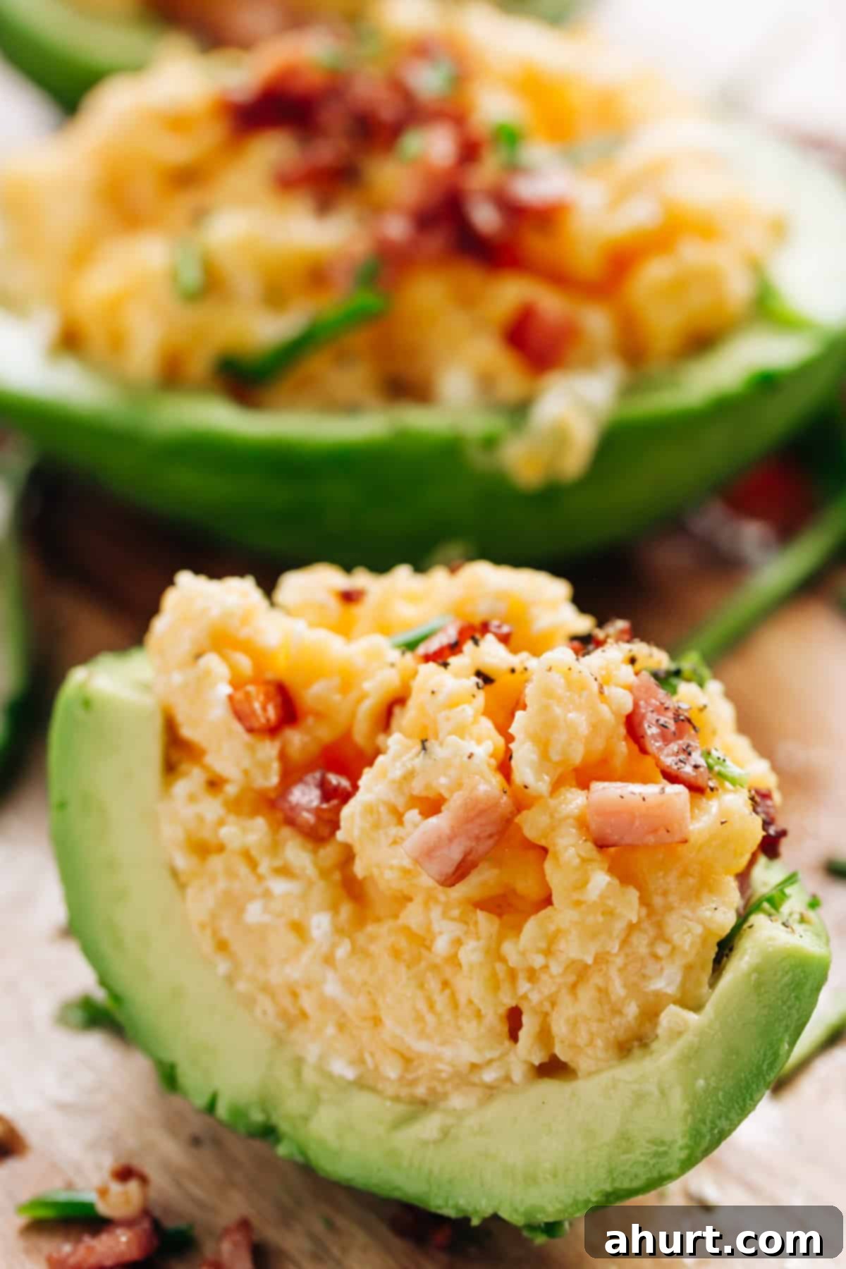 Avocado Scrambled Egg Boats 5 Side view of Scrambled eggs topped with bacon and cracked pepper, stuffed into half avocado, cut in half again to display inside.