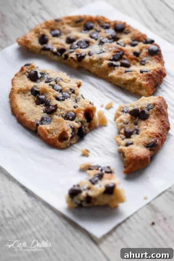 A close-up of a single serve jumbo low carb chocolate chip cookie broken into pieces, revealing its soft, fudgy interior and abundant chocolate chips, ready to be enjoyed.