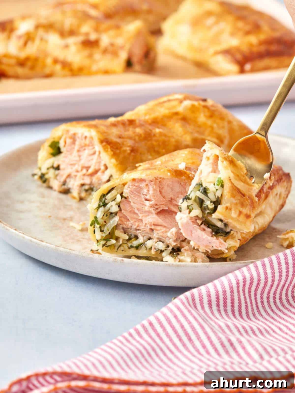 Flaky Salmon and Spinach Pockets 12 Serving a Puff Pastry Salmon Parcel on a plate, showing the crispy layers and juicy salmon filling being picked up with a fork.