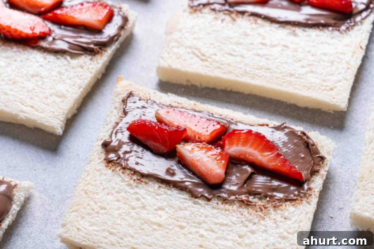 French Toast Rolls Breakfast Perfection 6 A close-up of sliced bread, half covered in Nutella and garnished with strawberries, ready to be rolled.
