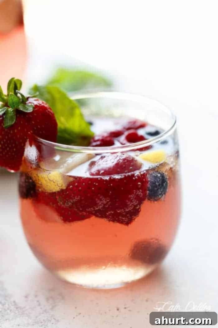A beautiful and refreshing spin on a traditional sangria using a mixture of frozen berries for a full berry flavor, a simple to make strawberry syrup, and the sweet Italian tangy-sweet citrus from limoncello! Berry Moscato Sangria in a pitcher and glasses with berries and mint.