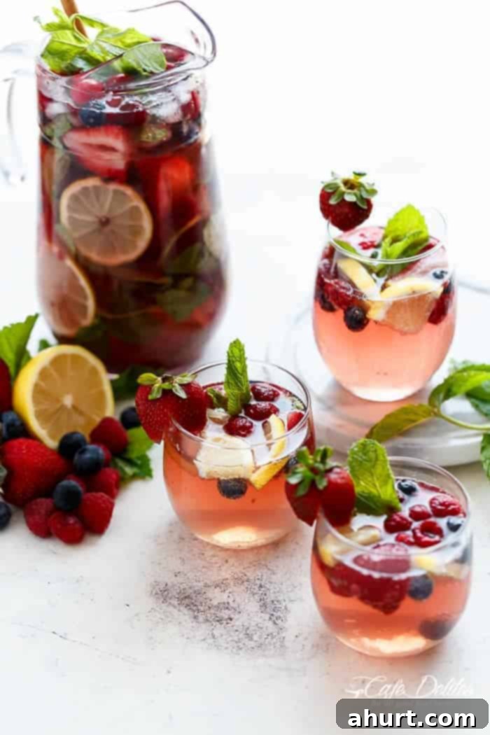 Three glasses and a pitcher filled with Berry Sangria, garnished with mint, ready for a celebration.