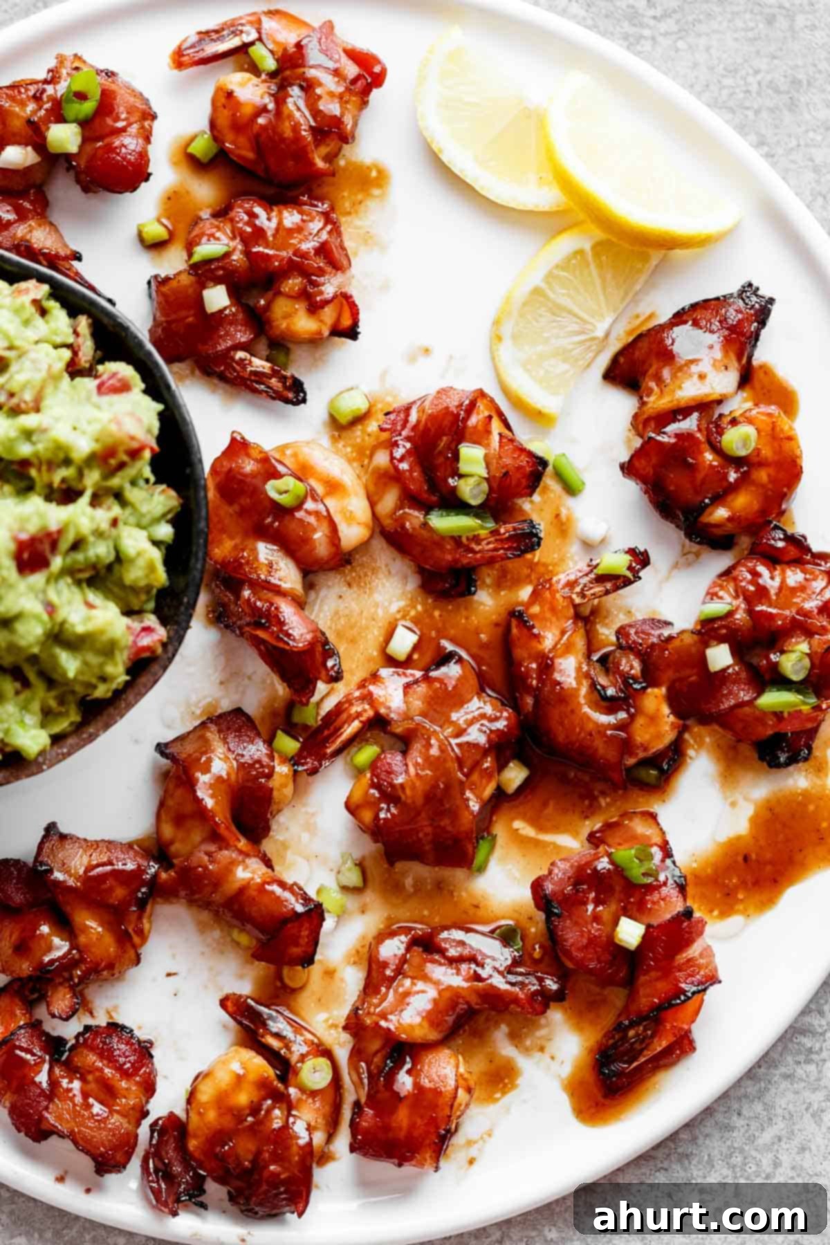 bacon wrapped shrimp #bacon #shrimp #oven Crispy and spicy Bacon Wrapped Shrimp drizzled in a sticky Honey Garlic Sauce with a side of guacamole in a ramekin and three half slices of lemon.
