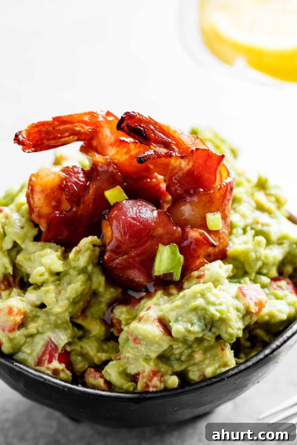 Creamy guacamole with bacon wrapped shrimp #guacamole #recipe #shrimp A bowl of flavorful guacamole with two glazed, wrapped prawns on top.