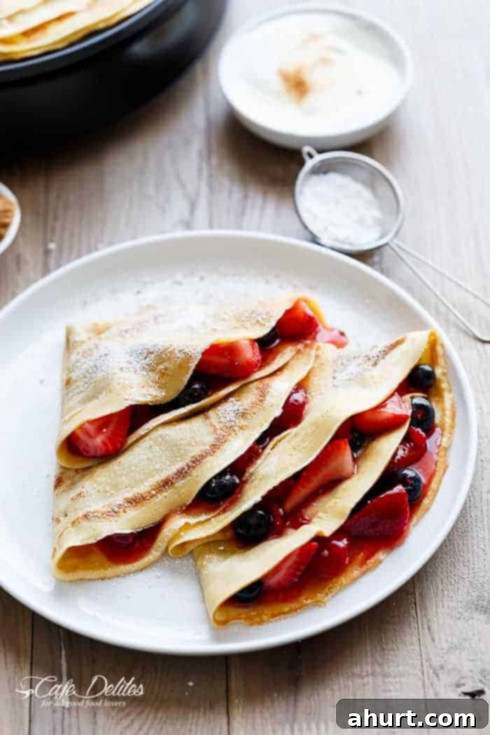 Stack of golden Blender Eggnog Crêpes on a plate, lightly dusted with powdered sugar and ready to be served