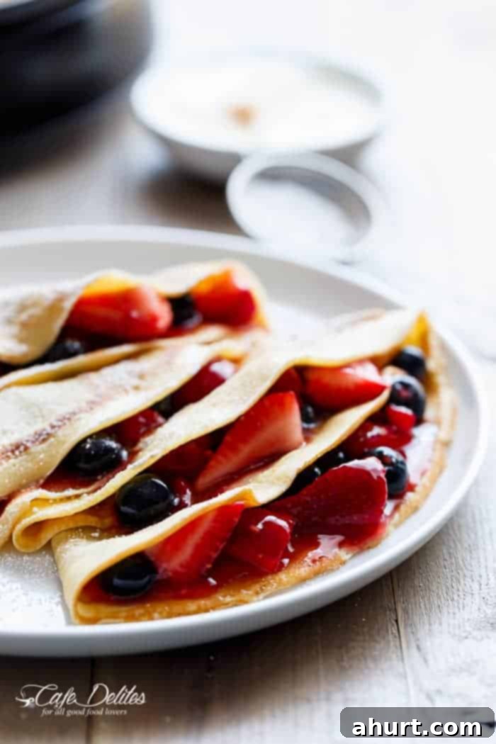 Plated Blender Eggnog Crêpes adorned with creamy cheesecake filling and fresh red and blue berries