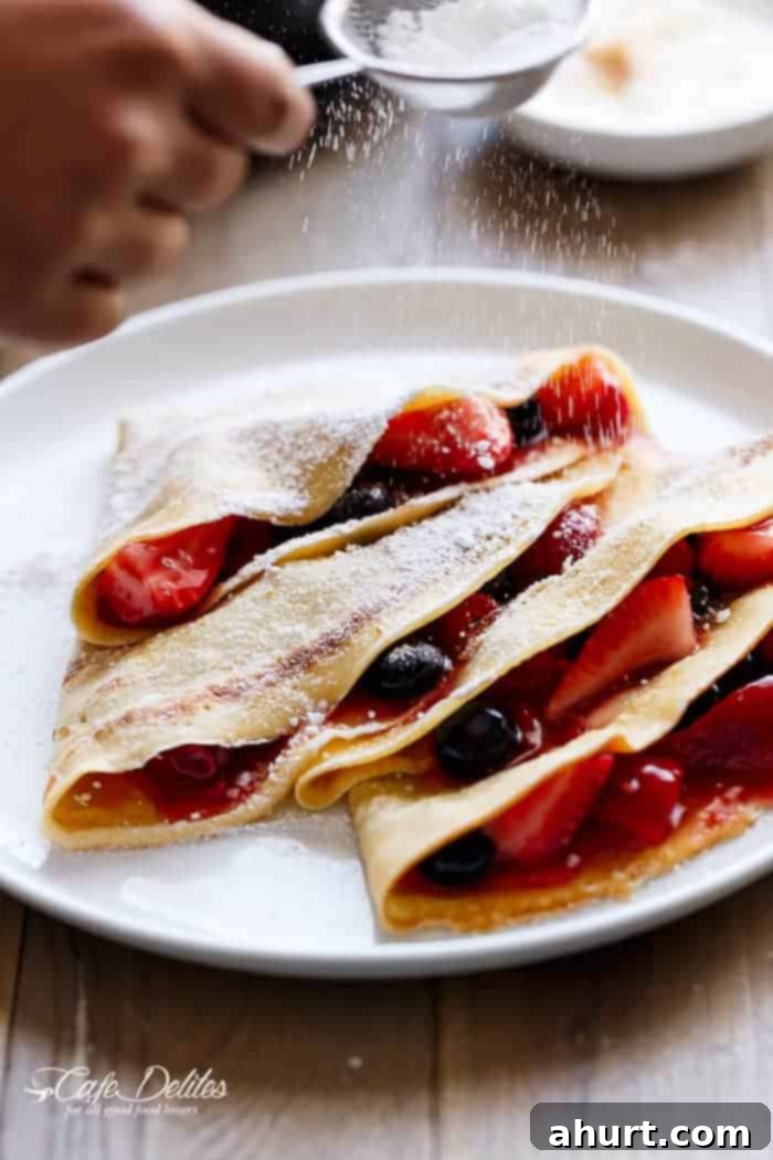 Two folded Eggnog Crêpes on a plate, garnished with fresh berries and powdered sugar, inviting and delicious