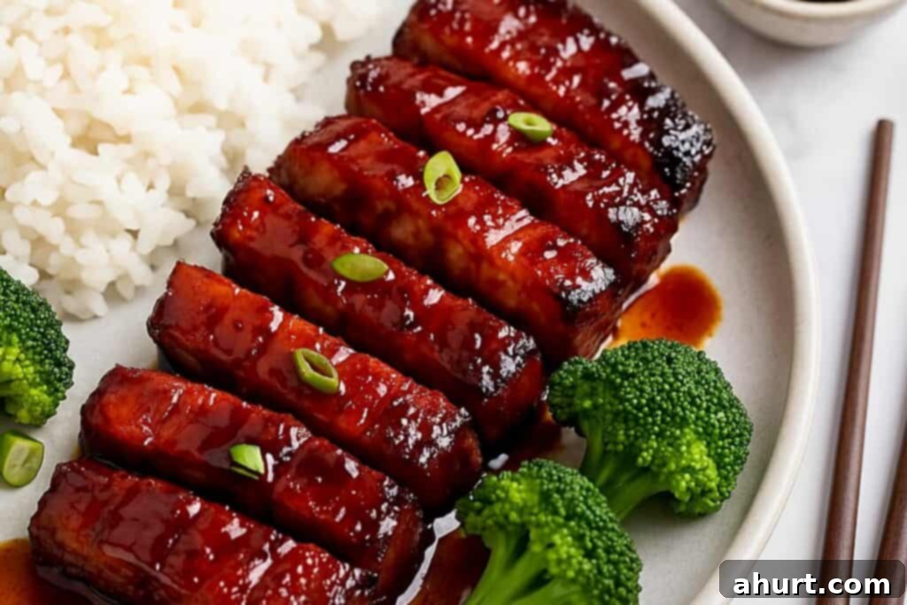 Glazed Char Siu Pork Belly 9 Char Siu pork belly served on a plate with steamed rice and vegetables, glossy glaze and charred edges visible, top-down view.