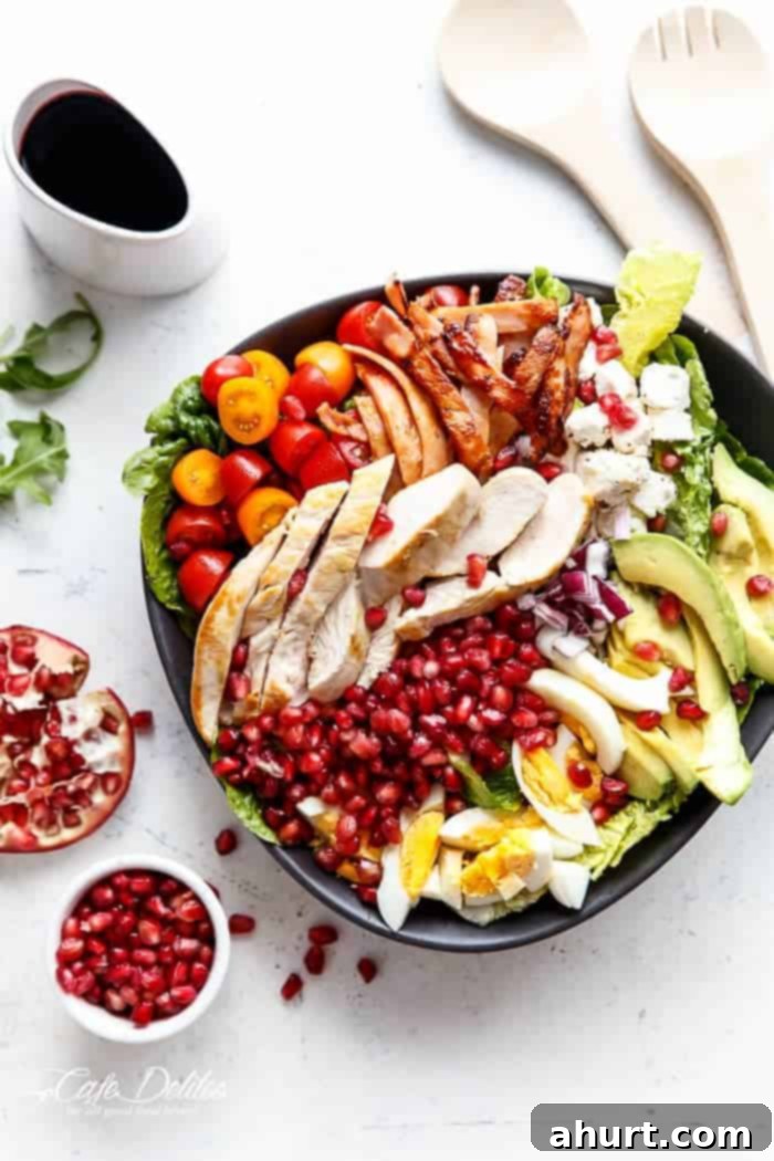 Jeweled Cobb Salad 2 Vibrant Pomegranate Cobb Salad in a large white bowl, showcasing crisp greens, chicken, bacon, avocado, eggs, tomatoes, feta, and ruby red pomegranate arils from a top-down view.