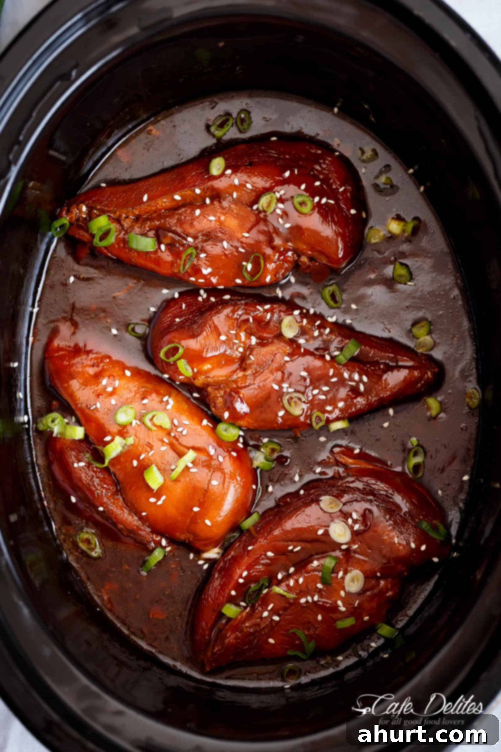 Cooked Slow Cooker Asian Glazed Chicken Breasts or chicken thighs simmering in a rich, dark sauce within a pan, ready for serving.