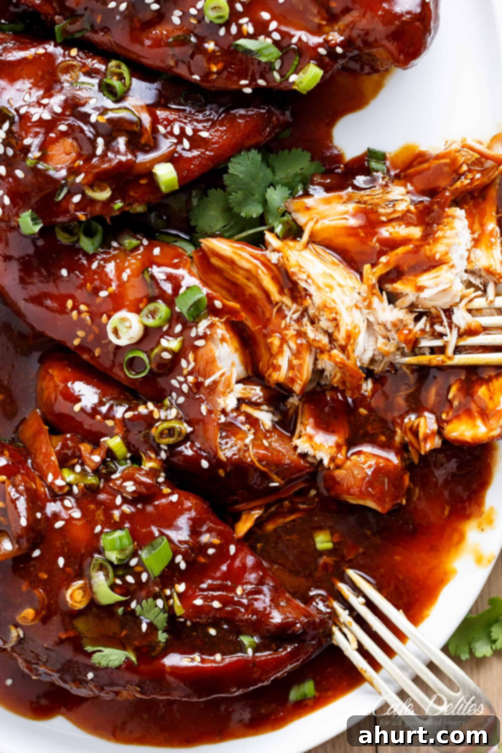 Close-up of Slow Cooker Asian Glazed Chicken Breasts garnished with green onions and sesame seeds, highlighting the sticky honey-garlic glaze.