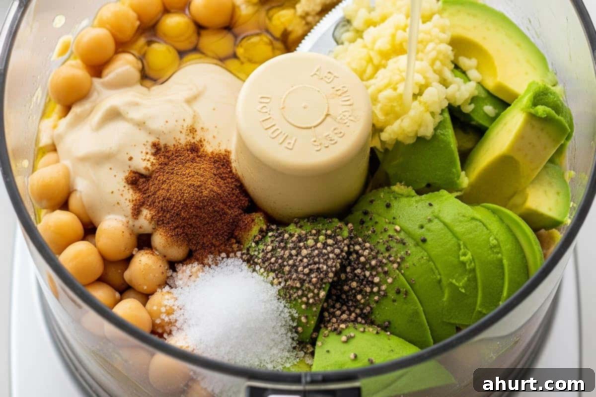 Creamy Avocado Hummus 6 All ingredients including chickpeas, tahini, lemon juice, olive oil, garlic, cumin, salt, pepper, and avocado in a food processor.