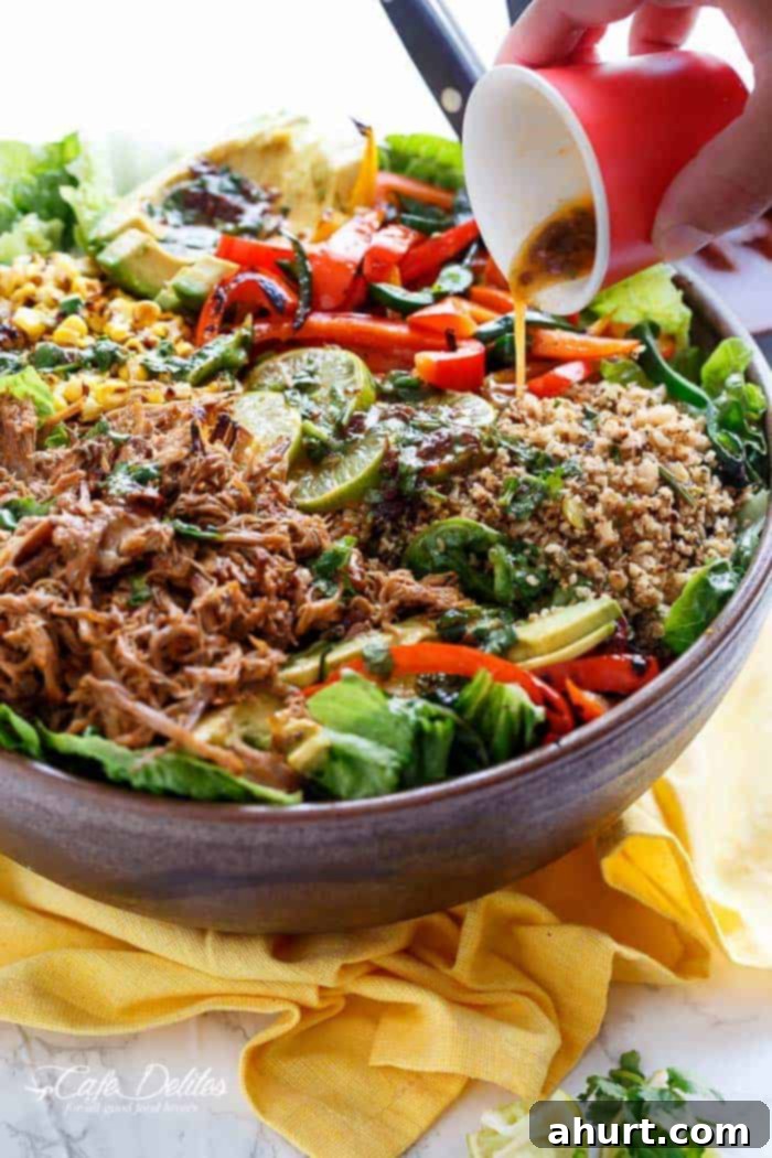 A large serving of Chipotle Lime Carnitas Salad generously drizzled with the homemade dressing, captured from a side angle.