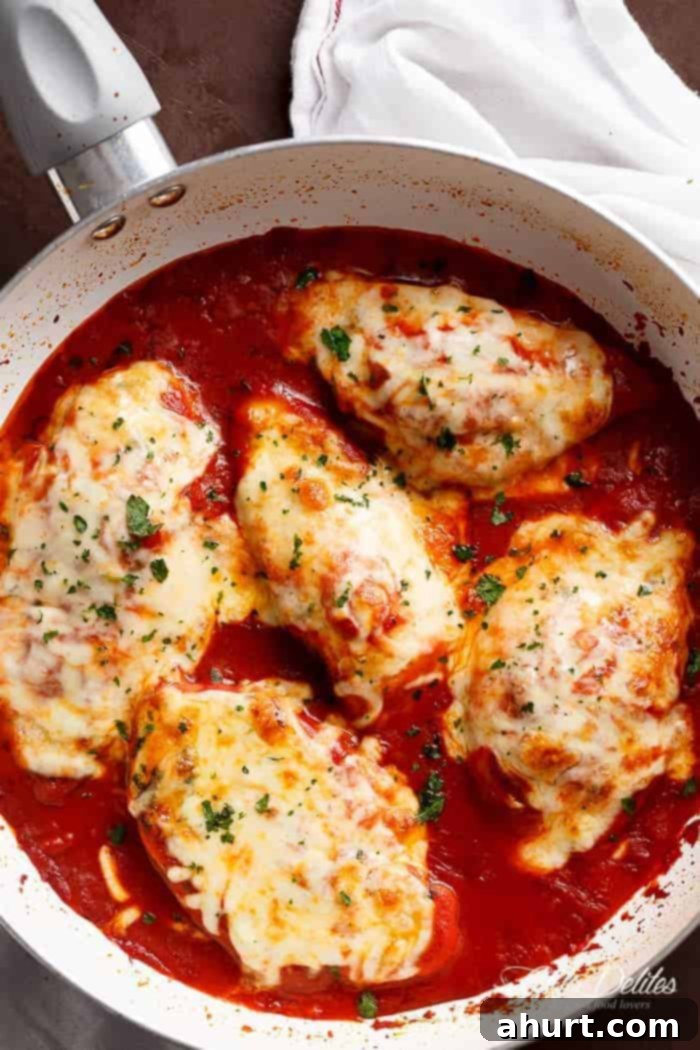 Chicken Mozzarella 2 Five pieces of golden-brown Mozzarella Chicken in a white pan, generously covered with melted, grilled mozzarella cheese and fresh green herbs, resting on a bed of vibrant tomato sauce.