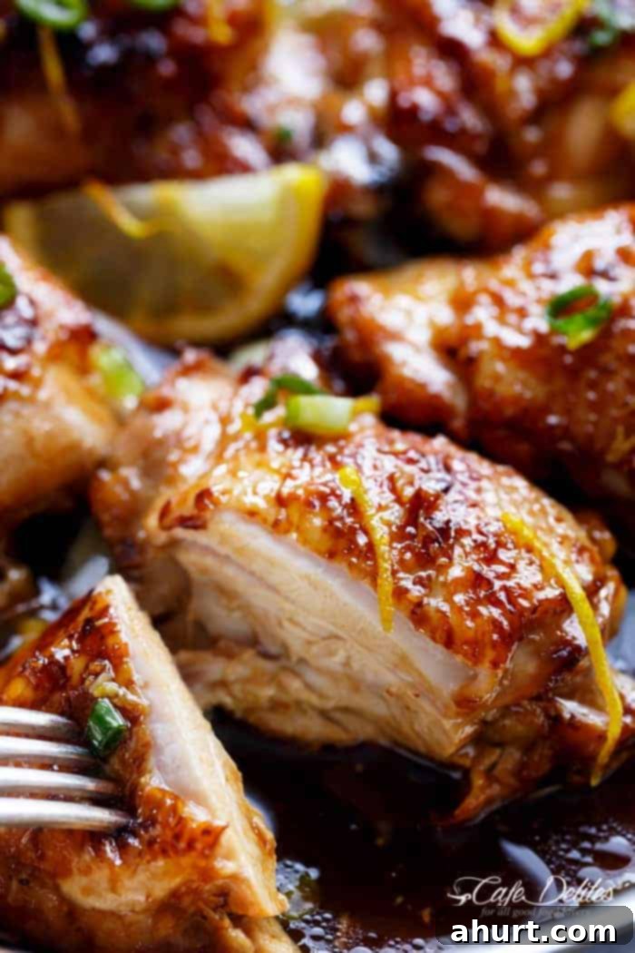 Close-up image focusing on a glistening piece of Honey Lemon Garlic Chicken, showcasing its crispy skin and sticky glaze.