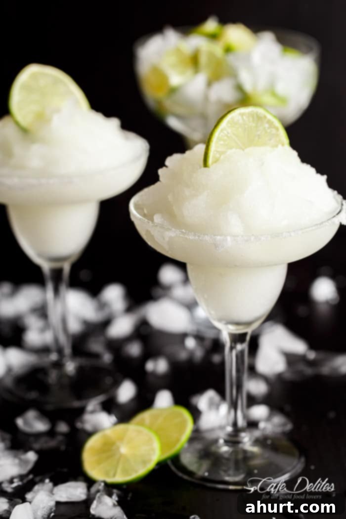 Blended Margarita Bliss 2 Two glasses of Fresh Frozen Margarita Slushies, each elegantly garnished with a round slice of lime, sitting on a table outdoors.