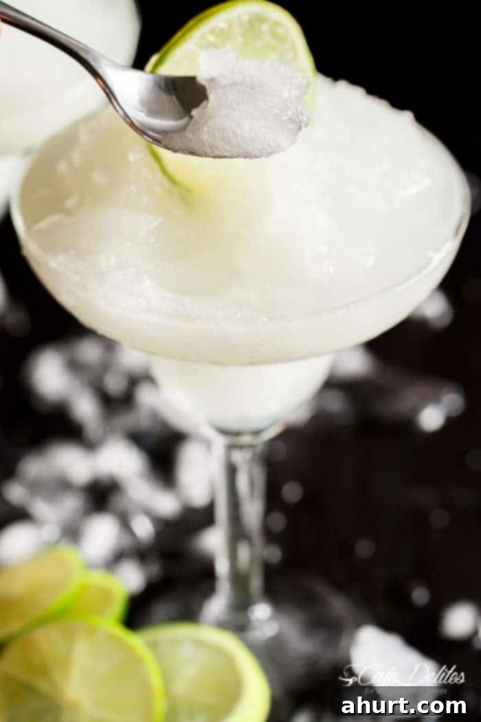Blended Margarita Bliss 6 Close-up of a silver spoon scooping delicious frozen slushy from a cocktail glass, highlighting the icy texture and lime garnish.