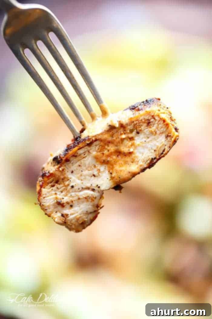 A fork lifting a piece of grilled Cajun chicken from the salad, showing its texture