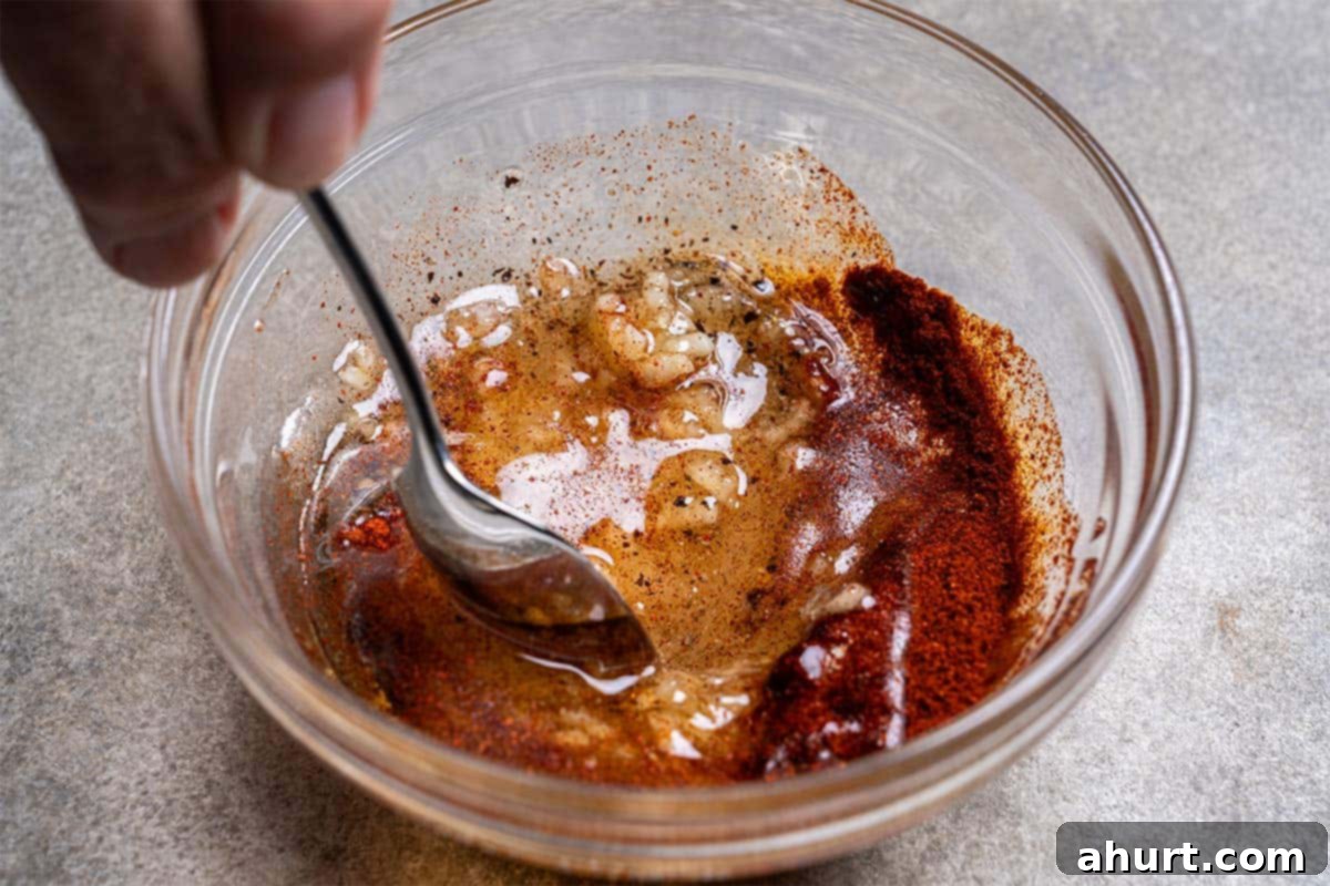 Oven-Roasted Crispy Garlic Potato Wedges 6 Oil, garlic, onion powder, salt, paprika, and pepper are being combined in a clear bowl with a spoon.