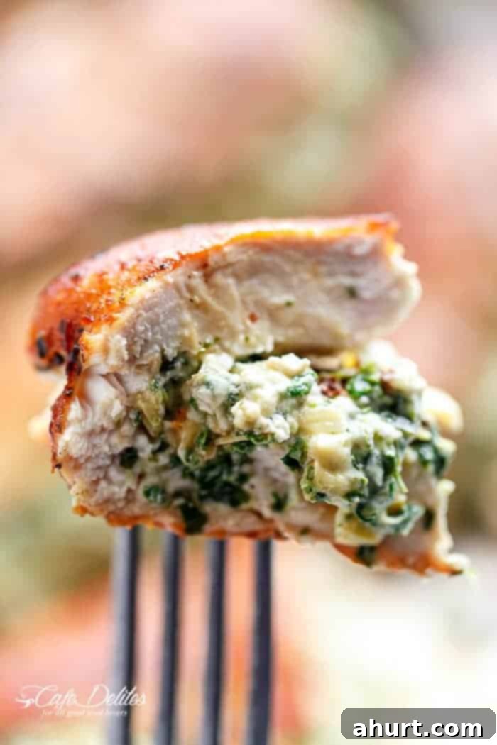 Cheesy Spinach Artichoke Stuffed Chicken 12 A fork taking a bite of Spinach Artichoke Stuffed Chicken, showing the creamy filling inside.