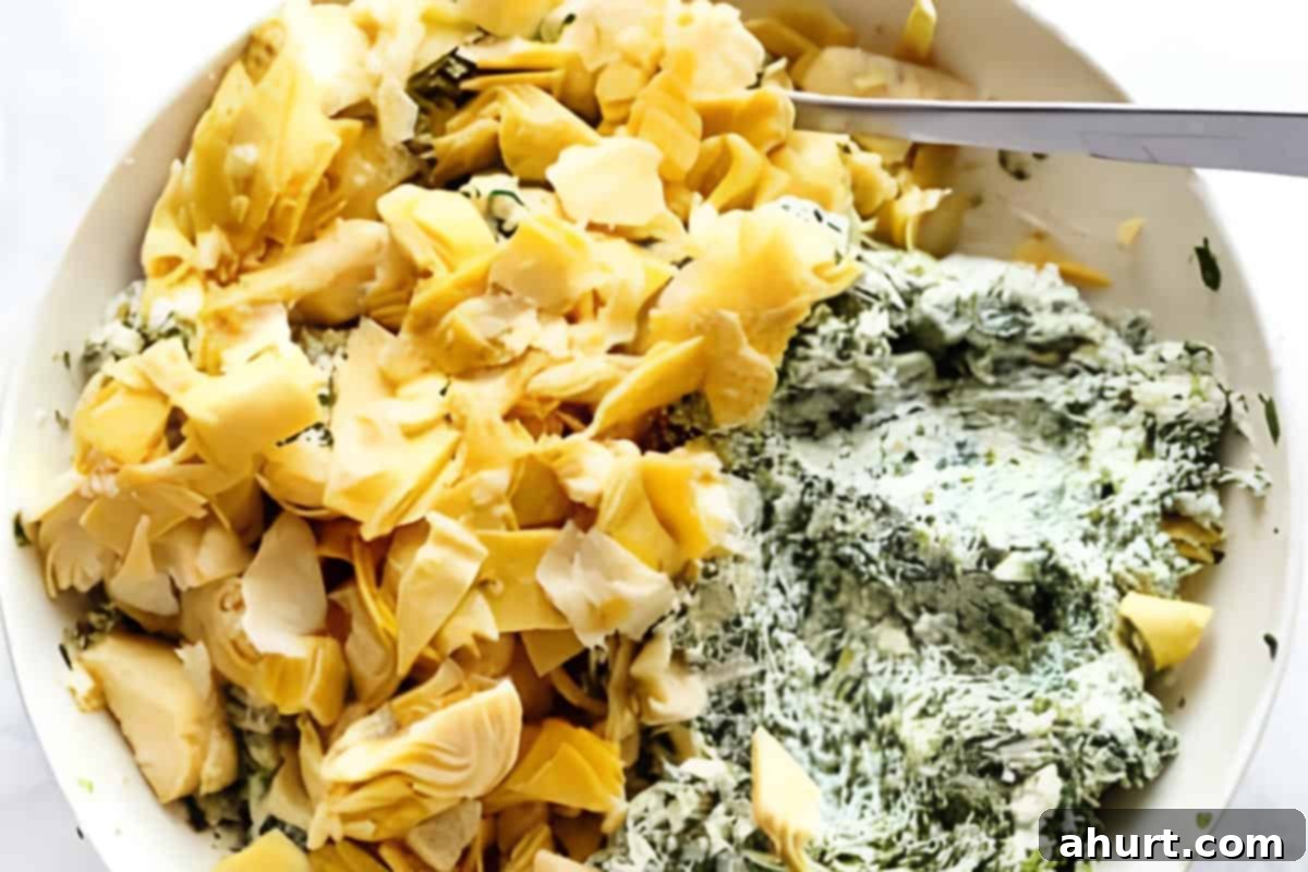 Cheesy Spinach Artichoke Stuffed Chicken 5 A bowl filled with a creamy spinach artichoke mixture, including cream cheese, chopped artichokes, mozzarella, parmesan, and minced garlic.