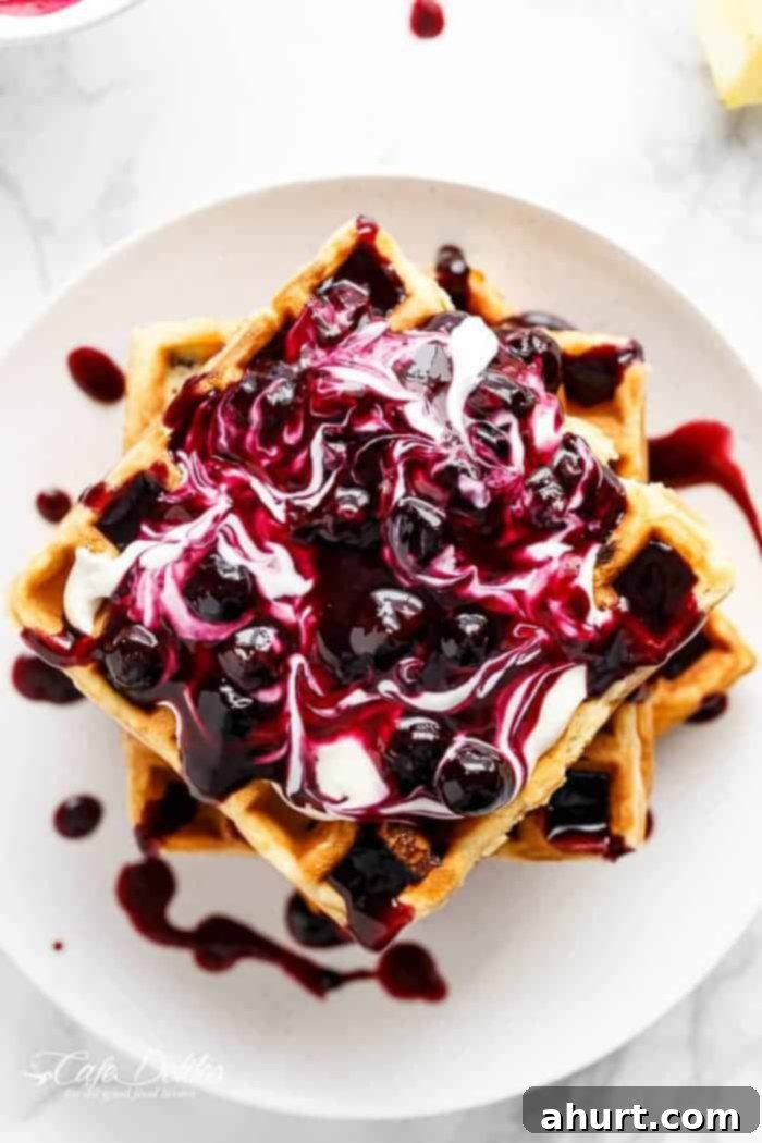 Homemade Blueberry Sauce generously poured over a stack of blueberry cheesecake waffles