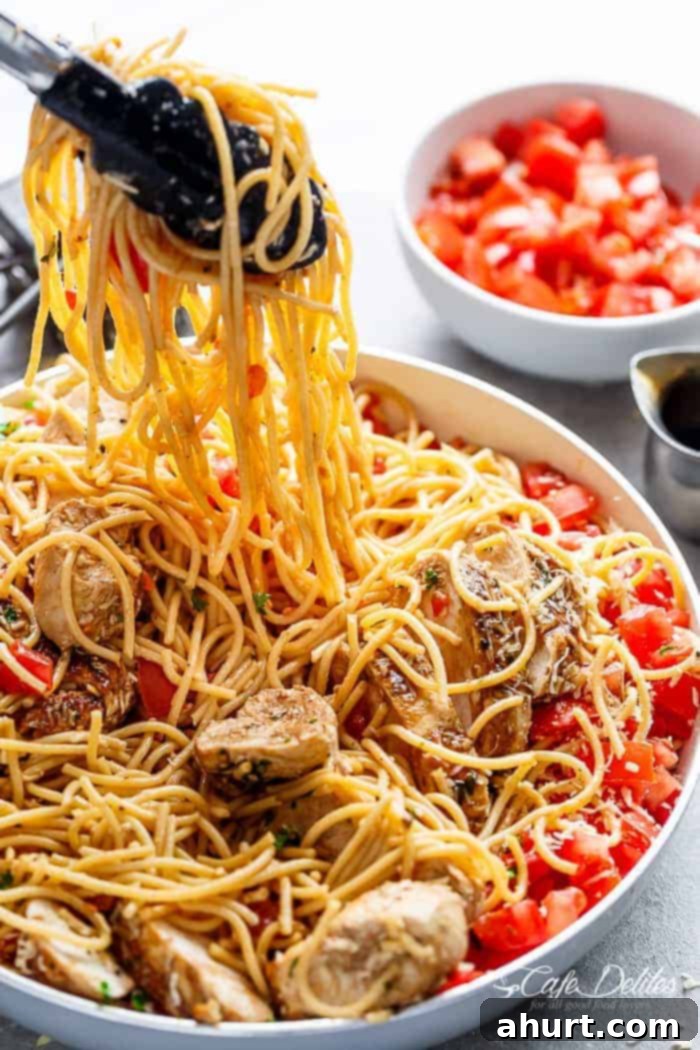 Summer Bruschetta Chicken Pasta Salad 4 Tong picking up the spaghetti from Bruschetta Chicken Pasta Salad is Filled with Italian seasoned grilled chicken, garlic and parmesan cheese!