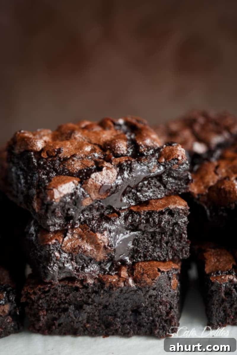 Decadent Cocoa Fudge Brownies 2 Side view of three slices of chocolate brownie stacked on top of each other. The brownies have a light brown top and dark, gooey interior.