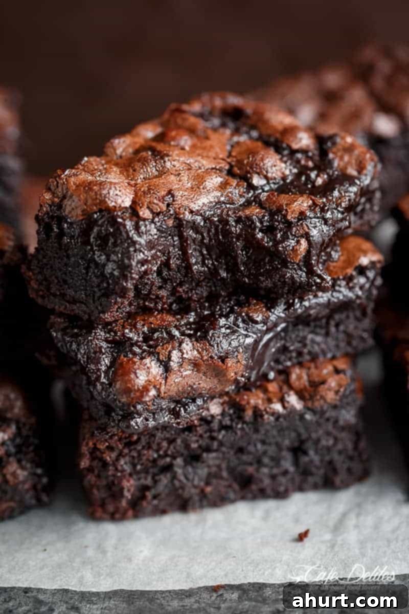 Decadent Cocoa Fudge Brownies 10 Image of three stacked fudgy brownies, one of which has a bite taken out of it.