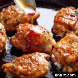 Sticky Honey Garlic Chicken 5 This close-up image of pan-seared chicken thighs coated in a vibrant orange glaze being drizzled with more of the glossy sauce from a spoon.