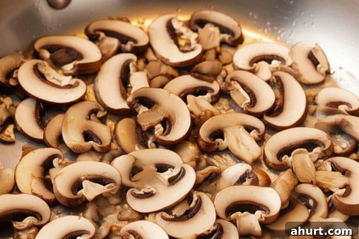 Luscious Creamy Garlic Parmesan Chicken 8 Sliced cremini mushrooms cooking with bacon and garlic in a skillet.