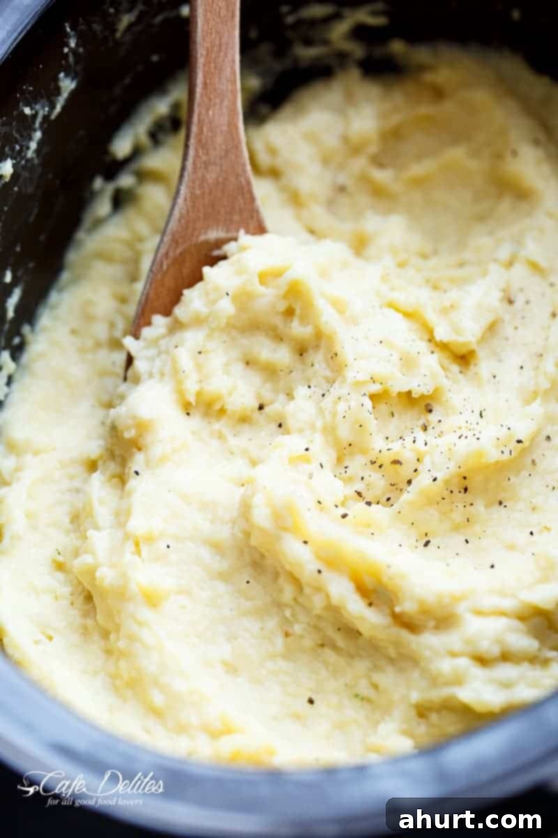 Creamy Slow Cooker Mashed Potatoes with a hint of garlic and parmesan cheese, served in a bowl with a wooden spoon.