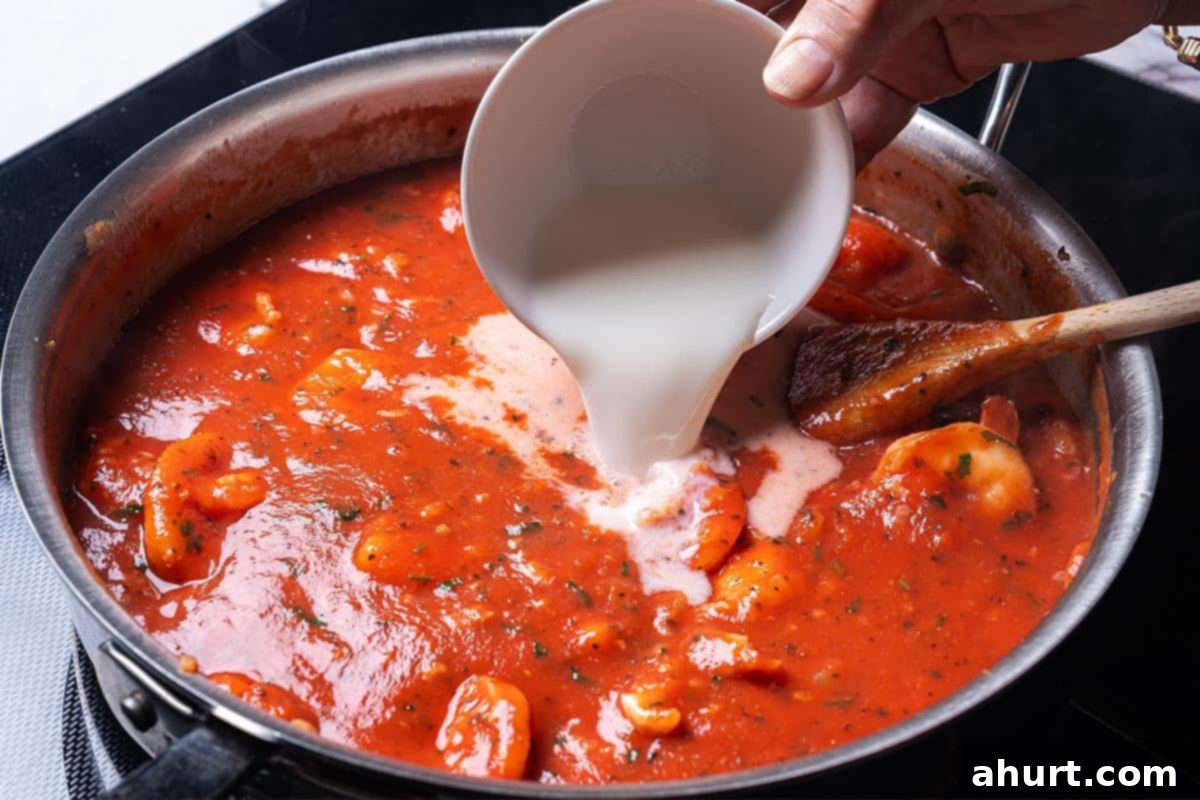 Velvety Tomato Garlic Butter Shrimp, Ready in 15 Minutes 7 Rich red marinara sauce in a skillet with heavy cream being poured in, creating a creamy texture