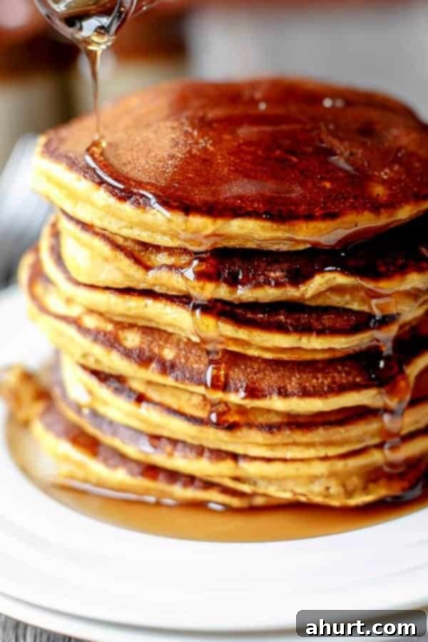 Close-up side view of a stack of three Caramel Chip Pumpkin Pancakes, revealing the soft, fluffy interior and melted caramel chips, with a slight drizzle of maple syrup.