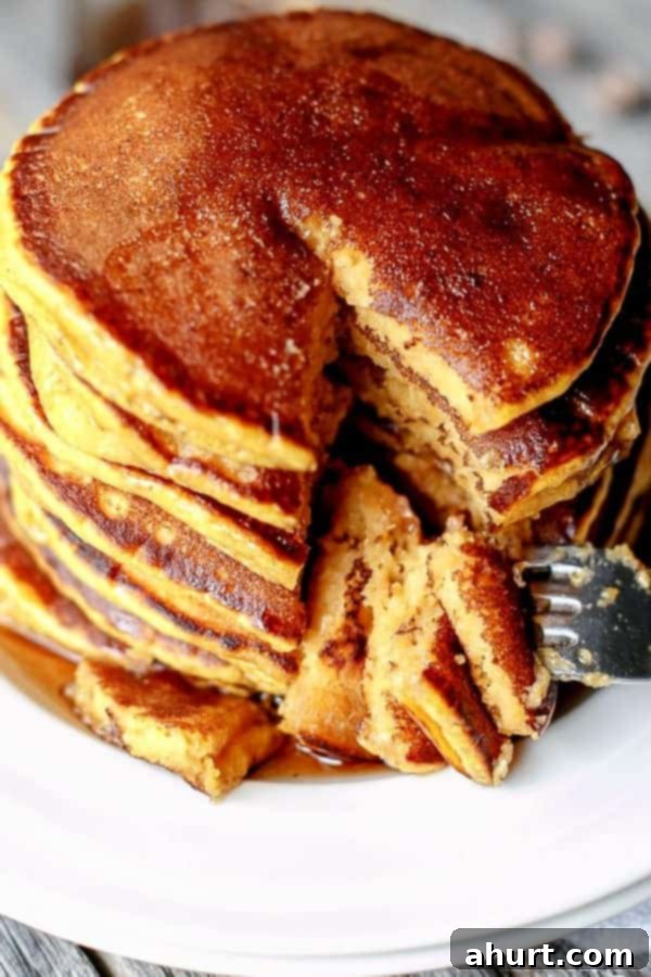 A fork is piercing a piece of a fluffy Caramel Chip Pumpkin Pancake, showing its soft interior and melted caramel, against a blurred background of the stack.