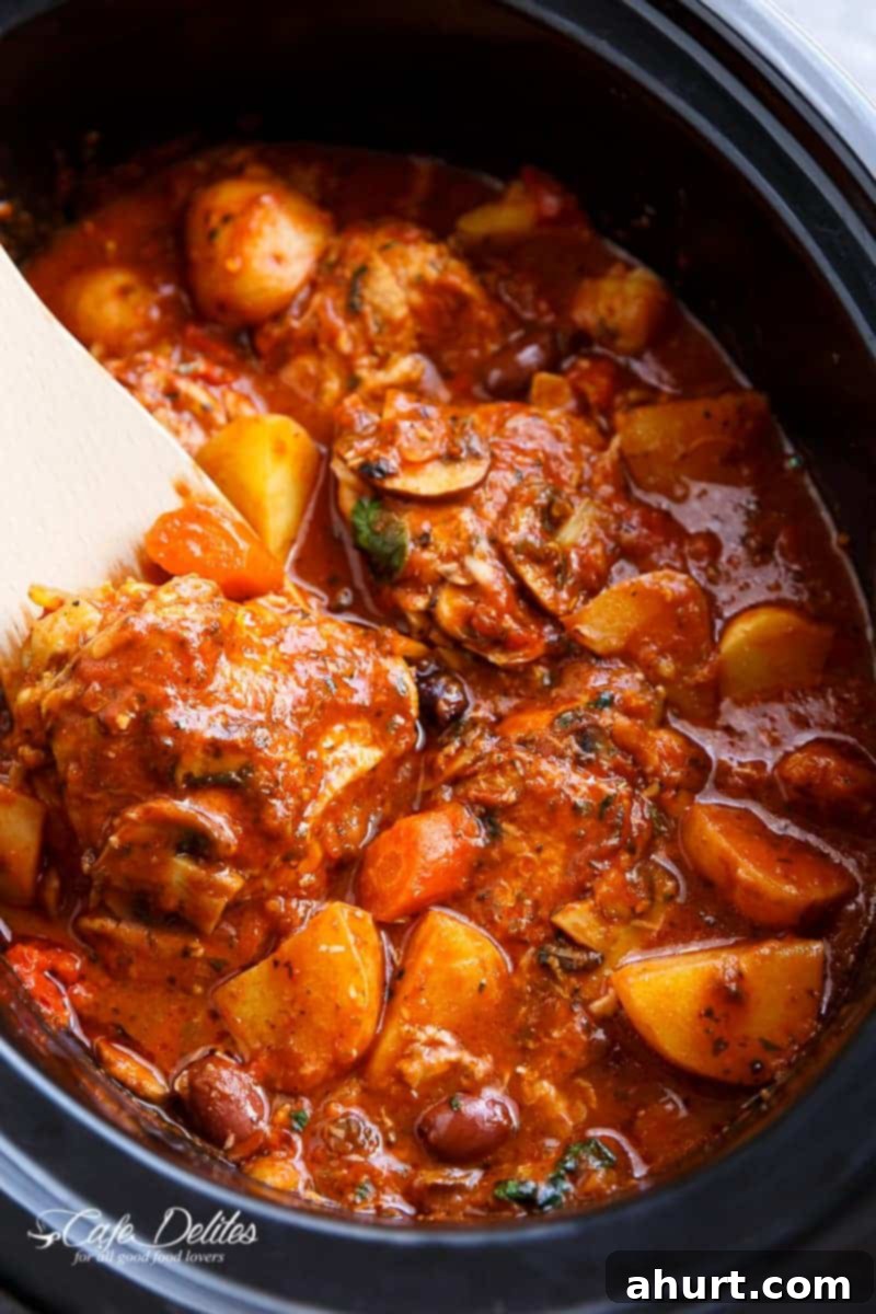 Set It and Forget It Chicken Cacciatore 2 A rich, red stew full of chicken, roughly chopped vegetables being stirred by a white spatula in a slow cooker.