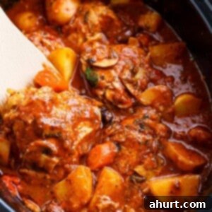 Set It and Forget It Chicken Cacciatore 5 A rich, red stew full of chicken, roughly chopped vegetables being stirred by a white spatular in a slow cooker.