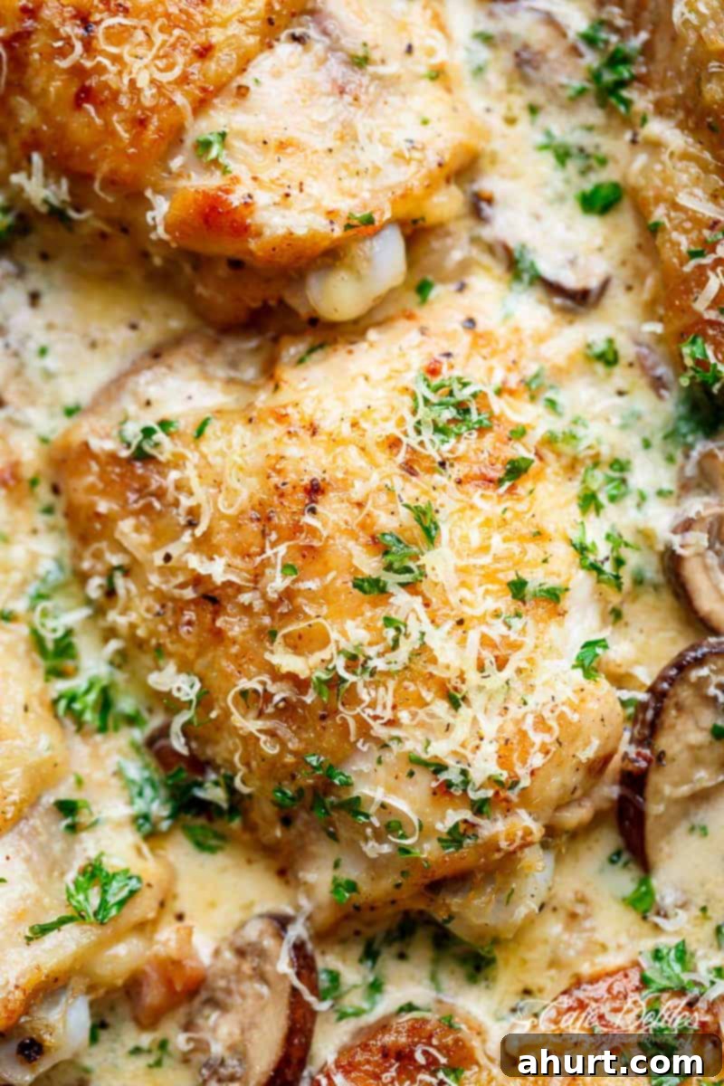 Close-up zoom on a piece of Creamy Parmesan Herb Mushroom Chicken in a pan with rich sauce and sliced mushrooms