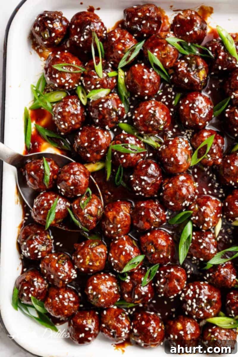 Sweet and Savory Mongolian Meatballs 2 Close-up of golden brown Mongolian Glazed Meatballs garnished with sesame seeds and green onions on a white plate