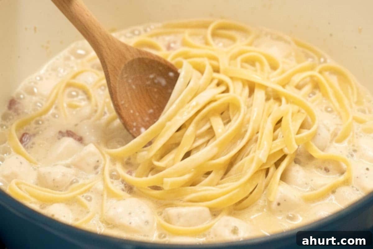 Easy One Pot Chicken Bacon Fettuccine Alfredo 8 Stirring the fettuccine pasta into the milk and chicken-bacon mixture with a wooden spoon as it begins to soften.