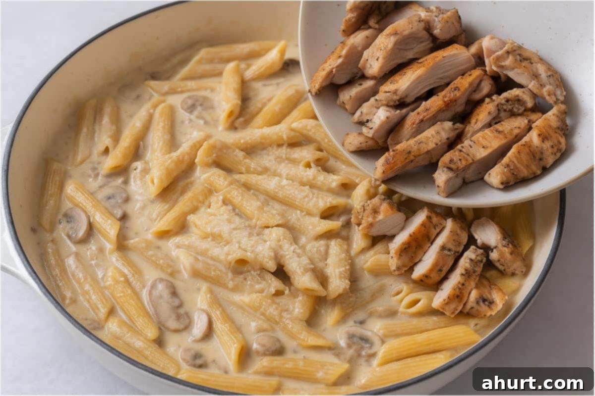 One-Pot Creamy Mushroom Chicken Pasta 7 Creamy mushroom sauce with penne being poured in with parmesan cheese and chicken thigh