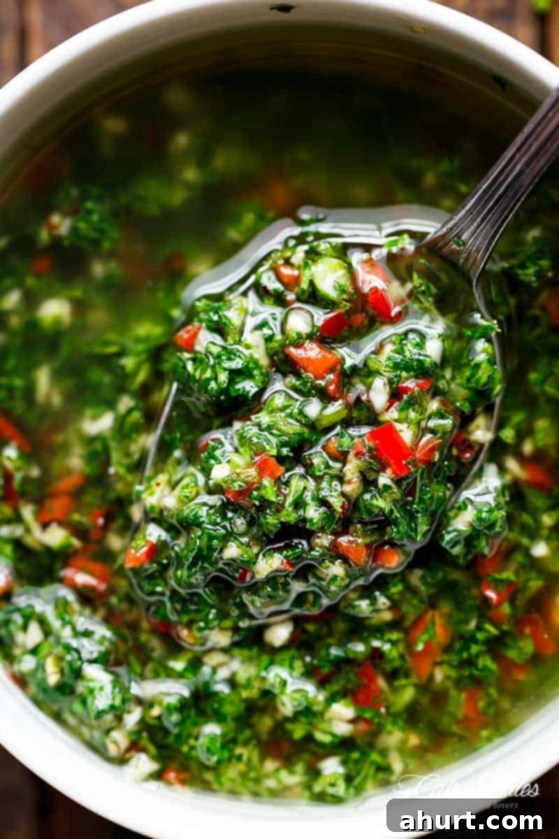 The Authentic Chimichurri of Uruguay and Argentina 2 A small serving spoon lifts a spoonful of vibrant chimichurri, showcasing green herbs and red chili pieces mixed with oil from a bowl.