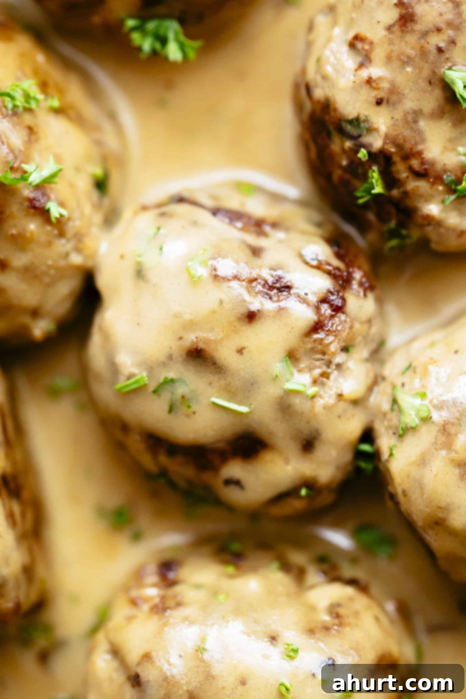 A close-up of a bowl filled with creamy Swedish meatballs, garnished with fresh herbs, showcasing the rich gravy.