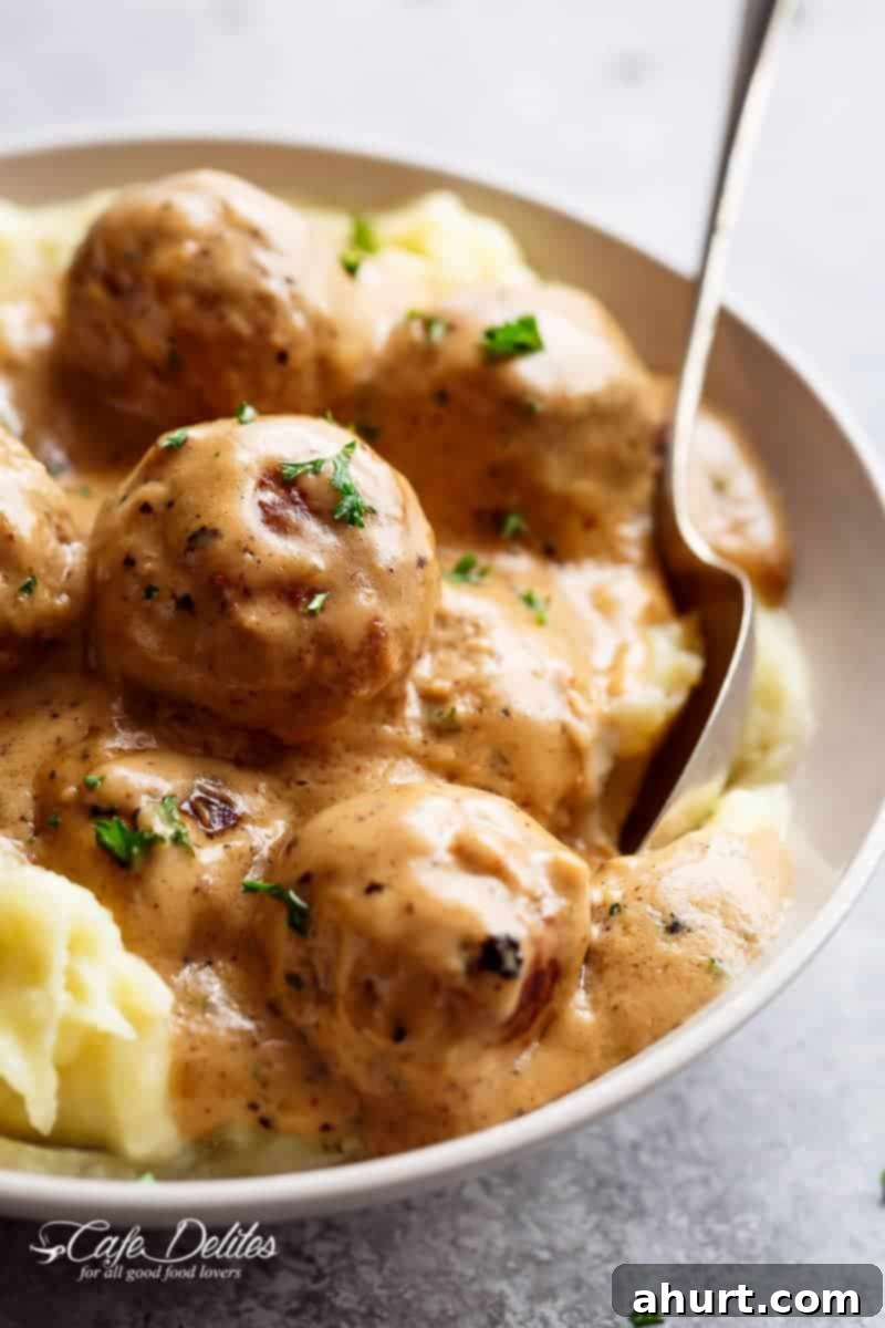 A close-up of the best Swedish meatballs served in a white bowl with a spoon, showing the rich gravy and tender meat.