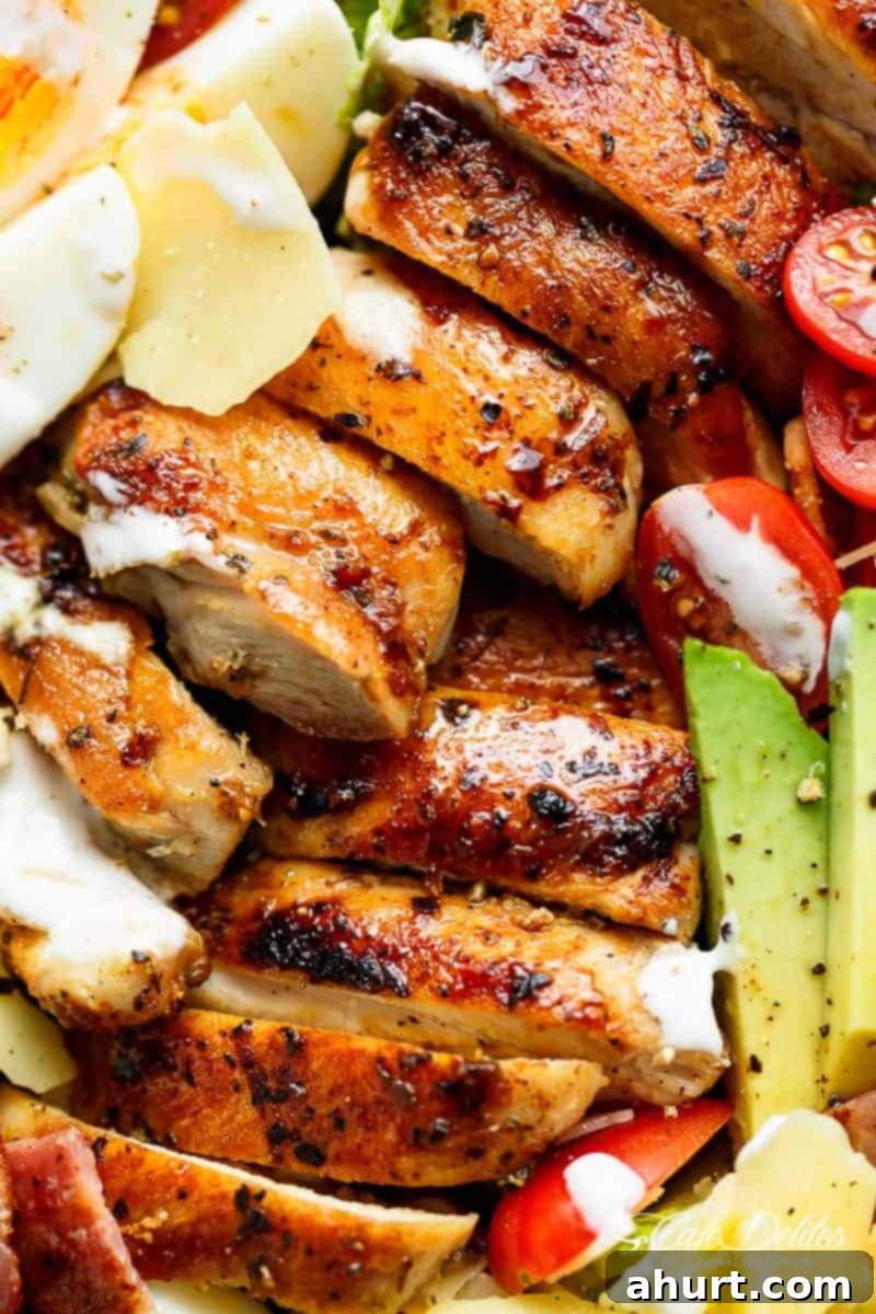 An enticing close-up of Grilled Chicken Cobb Caesar Salad, highlighting the rich textures of chicken, avocado, and perfectly cooked egg.