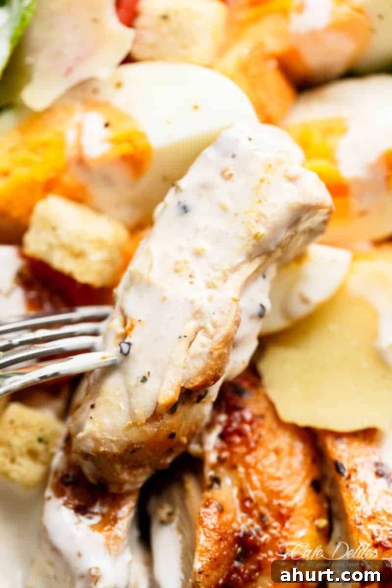 A fork lifts a juicy piece of grilled chicken from the Grilled Chicken Cobb Caesar Salad, ready to be enjoyed.