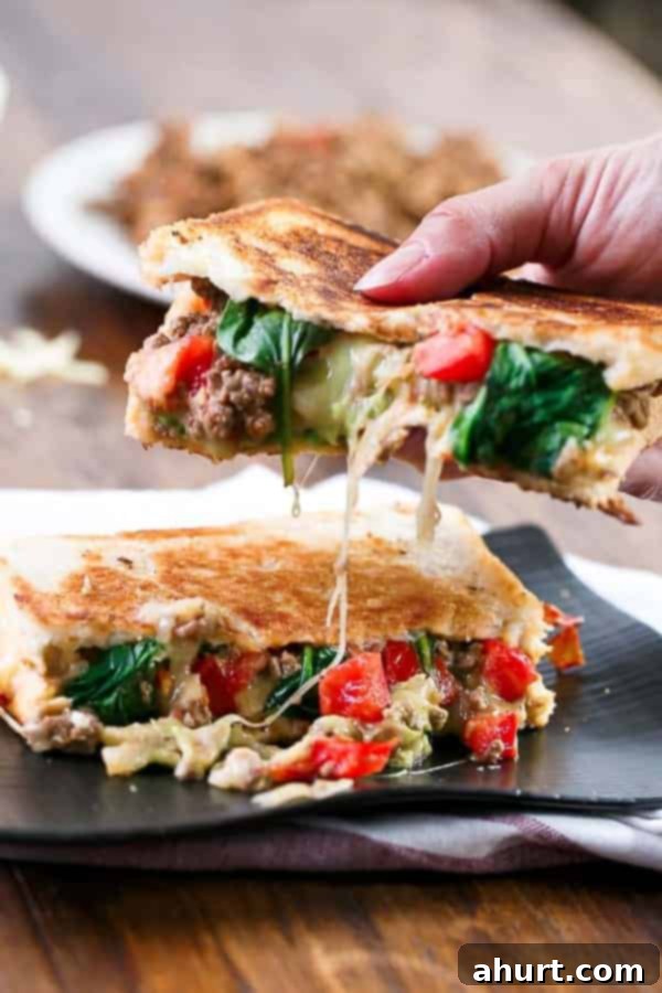 A hand holding a Loaded Taco Grilled Cheese sandwich, showing its hearty size and delicious layers.